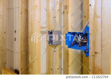 Located on wall above wooden frame beam is plastic electrical switch box with wires 111822704