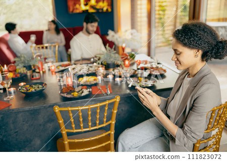 Group of friends chatting on mobile phones while sitting together at holiday dinner table at home Group of friends chatting on mobile phones while sitting together at holiday dinner table at home 111823072