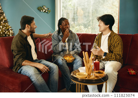 Cheerful young people eating snacks and talking while having Christmas home party together Cheerful young people eating snacks and talking while having Christmas home party together 111823074
