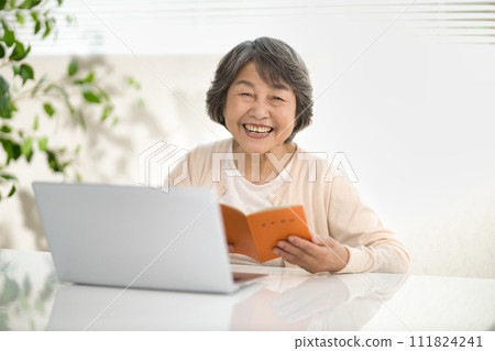 A senior woman using a computer while looking at her pension notebook, ending her life 111824241
