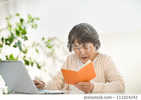 A senior woman using a computer while looking at her pension notebook, ending her life 111824242