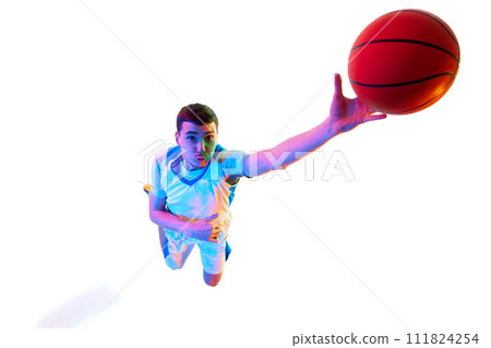 Overhead view of basketball player reaching out for slam dunk with enthusiasm against white studio background in neon light. Overhead view of basketball player reaching out for slam dunk with enthusiasm against white studio background in neon light. 111824254