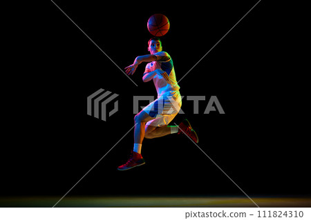 Action photo of young athlete man, basketball player doing pass against black studio background in mixed neon light. 111824310
