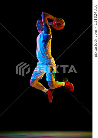 Basketball player doing layup to basket in action against black studio background in mixed neon light. Dynamic shot. 111824316