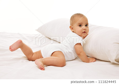 Portrait of beautiful little baby girl, toddler in onesie posing on bed against white background. Healthcare and education 111824445