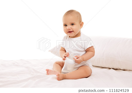 Little baby child, girl, adorable infant in white onesie sitting on bed with pillow and smiling against white background Little baby child, girl, adorable infant in white onesie sitting on bed with pillow and smiling against white background 111824529