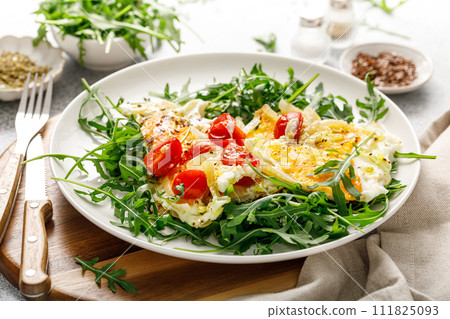 Fried eggs, omelette with onions, tomatoes and fresh arugula salad 111825093