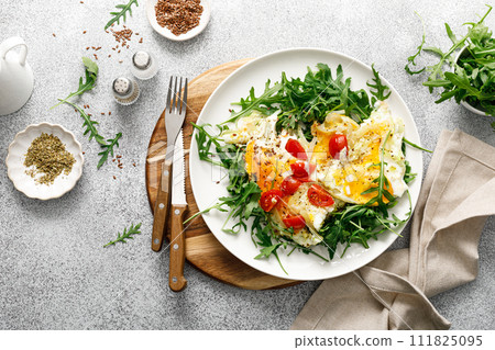 Fried eggs, omelette with onions, tomatoes and fresh arugula salad, top view 111825095