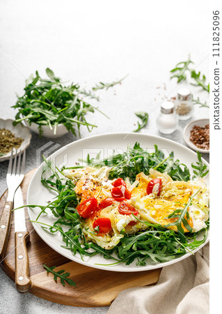Fried eggs, omelette with onions, tomatoes and fresh arugula salad Fried eggs, omelette with onions, tomatoes and fresh arugula salad 111825096