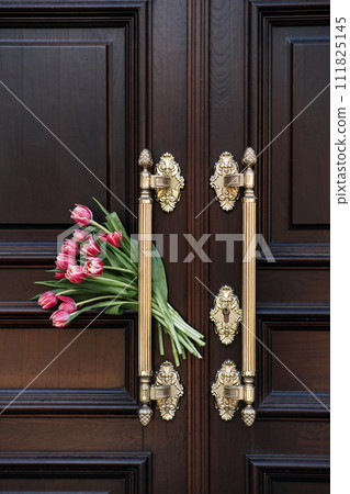 Welcome and Hospitality. Tulips bouquet Beside Ornate Wooden Door Welcome Symbol. The flowers next to a door symbolize a warm welcome or hospitality in home or upscale venue. Welcome and Hospitality. Tulips bouquet Beside Ornate Wooden Door Welcome Symbol. The flowers next to a door symbolize a warm welcome or hospitality in home or upscale venue. 111825145