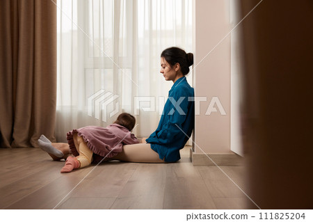tired woman sitting on the floor with her little child girl at home tired woman sitting on the floor with her little child girl at home 111825204