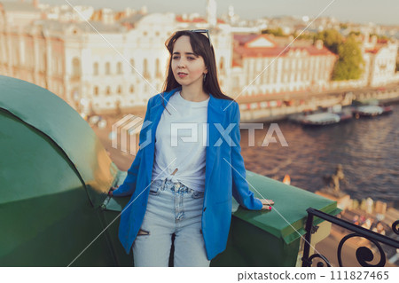 Young happy woman in jeans and blue jacket sits resting on rooftop in St Petersburg 111827465