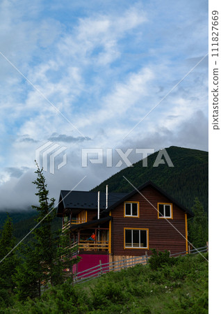 A large wooden house for tourists in the mountains, a young girl stands on the terrace against the background of the Carpathian mountains. 111827669