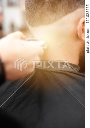 Barber shaves the temple with cordless trimmer during a short haircut on the sides of the head. 111828235
