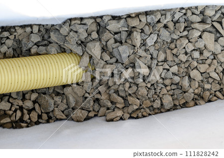 Yellow corrugated pipe with perforation in a trench with crushed stone and geotextile. Drainage works for the removal of ground water. 111828242