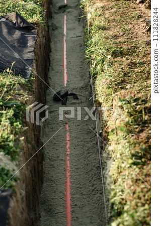 An orange reinforced sewer pipe is compacted with sand in a trench. Plumbing works on private plot. 111828244