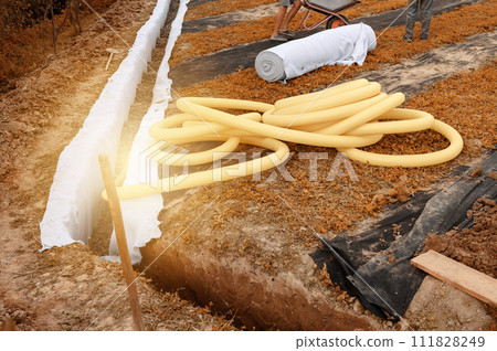 Yellow corrugated pipe with perforation in a trench with crushed stone and geotextile. Drainage works for the removal of ground water. 111828249