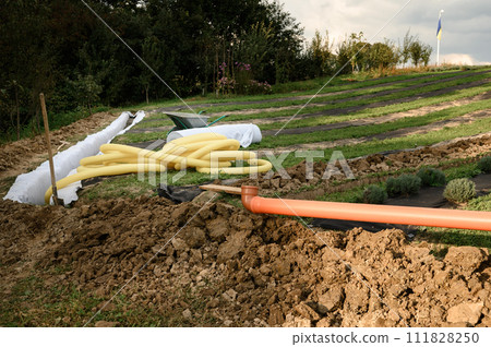 Yellow corrugated pipe with perforation in a trench with crushed stone and geotextile. Drainage works for the removal of ground water. 111828250