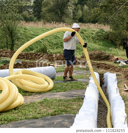 A worker carries a yellow perforated drainage pipe. Groundwater drainage works in the field A worker carries a yellow perforated drainage pipe. Groundwater drainage works in the field 111828255