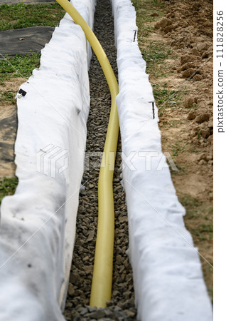 Yellow corrugated pipe with perforation in a trench with crushed stone and geotextile. Drainage works for the removal of ground water. Yellow corrugated pipe with perforation in a trench with crushed stone and geotextile. Drainage works for the removal of ground water. 111828256
