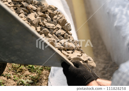 Drainage works for drainage of ground water. A man pours rubble crushed stone from a wheelbarrow into a trench close up. Drainage works for drainage of ground water. A man pours rubble crushed stone from a wheelbarrow into a trench close up. 111828258