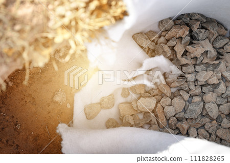 The drainage trench is covered with geotextile and filled with crushed stone to drain ground water from the site. The drainage trench is covered with geotextile and filled with crushed stone to drain ground water from the site. 111828265