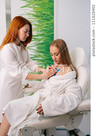 Vertical portrait of professional female cardiologist attaching holter sensors on woman patient with heart disease. Young woman during functional rehabilitation in cardiology room in clinic. 111828402