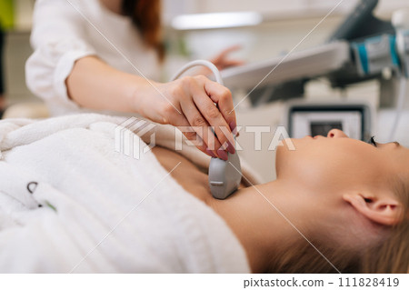 Closeup of beautiful woman examine thyroid gland with ultrasound probe in medical clinic. Close-up of unrecognizable female doctor holding ultrasound probe along patient neck. Shooting in slow motion. 111828419