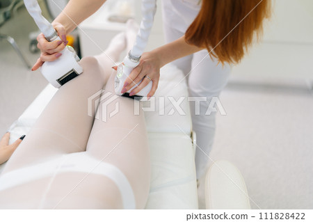 Top view of unrecognizable female patient wearing white suit having anti-cellulite LPG massage. Professional woman masseur doing massage with LPG apparatus machine for lifting body in beauty salon. 111828422