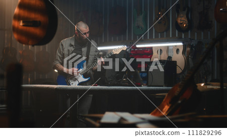 Male craftsman plays guitar connected to combo amp, checks the sound Male craftsman plays guitar connected to combo amp, checks the sound 111829296