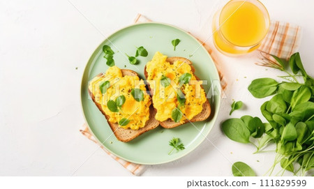 Fresh scrambled eggs on toast with microgreens and a glass of orange juice on a light background. 111829599