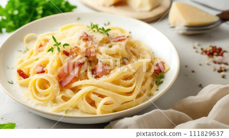 Creamy fettuccine pasta with bacon and parmesan on a white plate, garnished with parsley, on a light background Creamy fettuccine pasta with bacon and parmesan on a white plate, garnished with parsley, on a light background 111829637