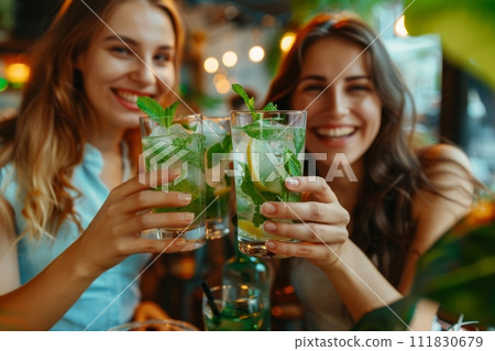 Two women are smiling and toasting with alcoholic beverages at a restaurant 111830679