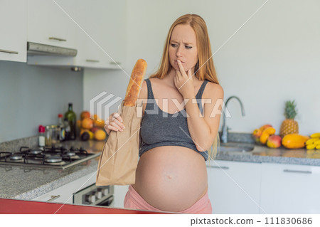 Pregnant woman eating bread in the kitchen. Exploring the impact of gluten during pregnancy: understanding the potential benefits and risks for maternal health and fetal development 111830686