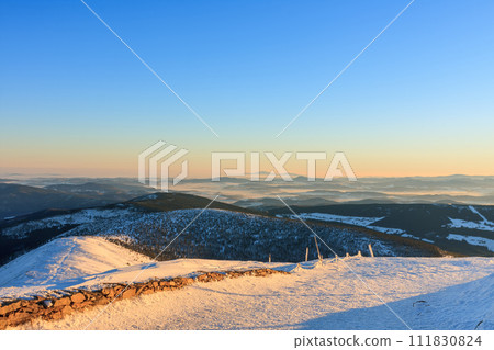 Winter, sunrise time, view from Snezka to pink mountain, krkonose mountain, Czech republic.. Along the road are wooden long bars, tourist markings for winter season. Winter, sunrise time, view from Snezka to pink mountain, krkonose mountain, Czech republic.. Along the road are wooden long bars, tourist markings for winter season. 111830824