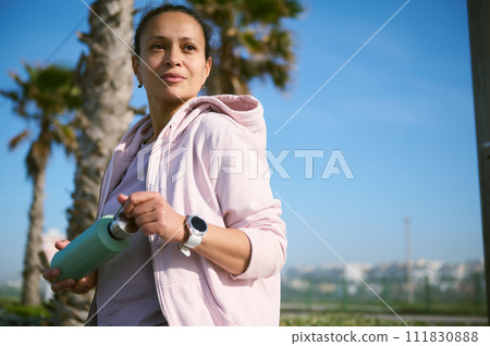 Confident young determined athlete holding a bottle of water, hydrating her body after intense outdoor workout. Confident young determined athlete holding a bottle of water, hydrating her body after intense outdoor workout. 111830888
