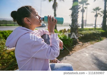 A woman is drinking water after training. A young and smiling girl is drinking a drink isotonic after physical fatigue. 111830907