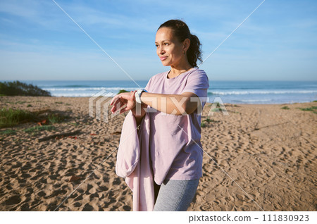 Happy female athlete wearing sports wear and checking her pulse rate with smartwatch while outdoors exercising 111830923