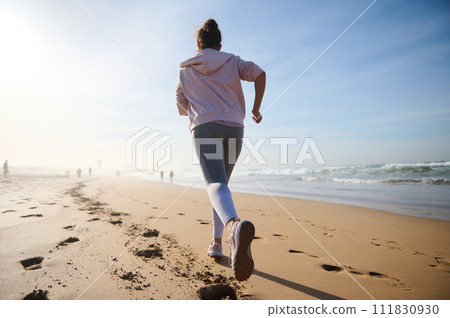 Determined strong young athletic woman, athlete, sportswoman during morning jog, running outdoors along Atlantic beach Determined strong young athletic woman, athlete, sportswoman during morning jog, running outdoors along Atlantic beach 111830930