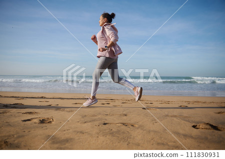 Full length side portrait of a sportive woman exercising outdoor, running jogging on the sandy beach on warm sunny day Full length side portrait of a sportive woman exercising outdoor, running jogging on the sandy beach on warm sunny day 111830931