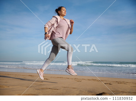 Active middle aged woman exercising outdoor, running along the Atlantic beach on warm sunny day in the morning 111830932