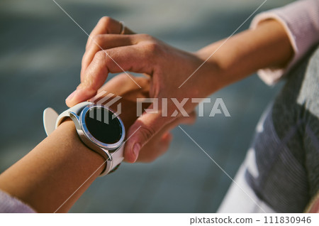 Close-up hands of female athlete checking application and heart rate on her smart watch during outdoor cardio workout 111830946