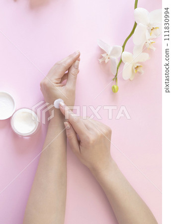Advertising of cosmetic cream. Hand cream, a woman smears her hands with cream on the background of white orchids. 111830994