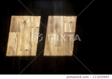 A shadow from the window. Sunlight from the window falls on the wooden floor. 111830997