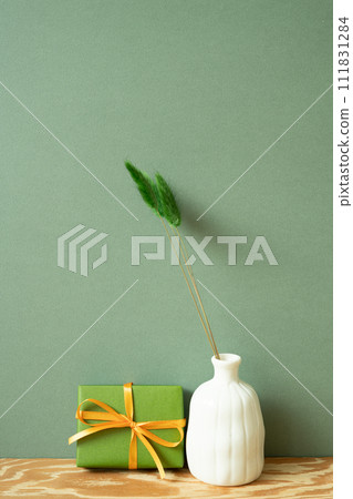 Green gift box and vase of dry flower on wooden table. green wall background Green gift box and vase of dry flower on wooden table. green wall background 111831284