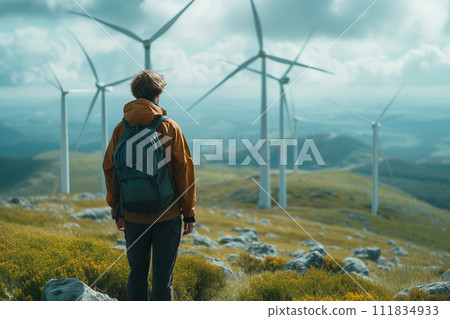 A lone hiker stands amidst a windswept hillside, gazing at towering wind turbines against a dramatic sky, a moment of reflection on sustainable energy within the natural landscape. 111834933