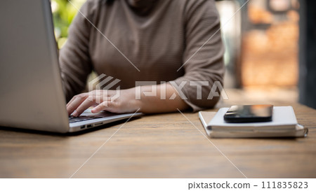 A cropped shot of a woman typing keyboard, working on her laptop computer at a table in a cafe. 111835823
