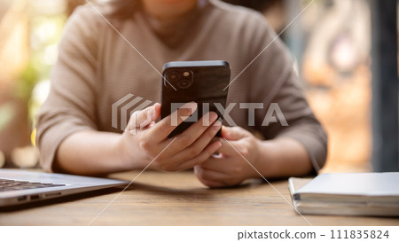 A cropped shot of an Asian woman responding to messages on her smartphone while sitting in a cafe. 111835824