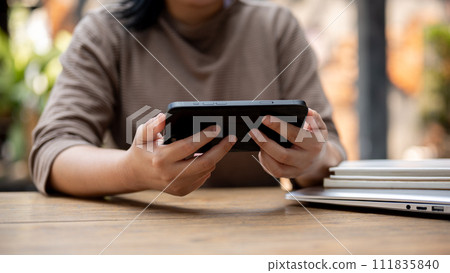 A cropped shot of an Asian woman watching videos on her smartphone while sitting in a cafe. 111835840