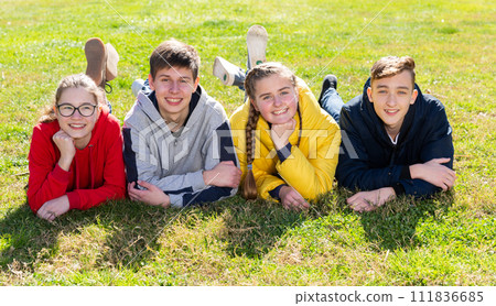Cheerful teen friends lying on green lawn Cheerful teen friends lying on green lawn 111836685